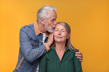 Senior man kissing his beloved woman on orange background