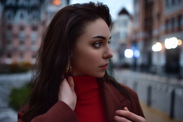 Dramatic close up portrait of young beautiful Girl looking aside against evening city background