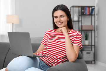 Happy young woman having video chat via laptop on sofa in living room