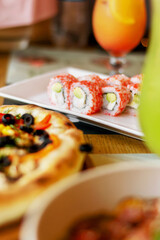 Delicious Sushi rolls with vegetarian pizza and cocktail in the background, in a cozy restaurant. Food, fast food, cafes
