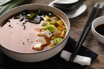 Bowl of delicious miso soup with tofu and chopsticks on wooden table, closeup