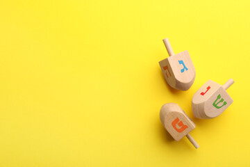 Wooden dreidels on yellow background, above view with space for text. Traditional Hanukkah game