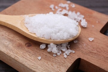 Spoon with sea salt on wooden board, closeup