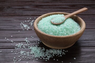 Bowl and spoon with turquoise sea salt on dark wooden table, closeup