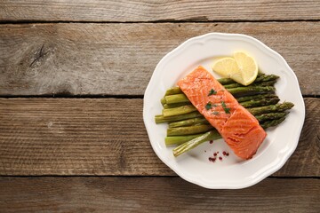 Tasty grilled salmon with asparagus and lemon on wooden table, top view. Space for text