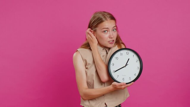 Woman with anxiety checking time on clock, running late to work, being in delay, deadline. Blonde busy girl looking at hour, minutes, worrying to be punctual isolated on pink studio background