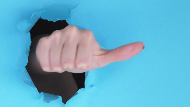 Vertical video. Like hand. Perfect choice. Accepting yes thumb up gesture through hole in breakthrough paper ripped wall on blue background with free space.