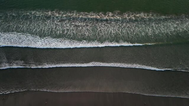 Aerial view of big ocean wave layers in Bali. Wavy beach with black sand during sunset or sunrise - Wide high angle, looking down 90 degree. 4k Cinematic video footage scene for opening or ending.