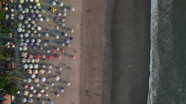 Aerial view of Beautiful sunset on the double six beach with Hotel, resort, cafe buildings, beach umbrella and calm ocean wave in Bali. Tourists are surfing, swimming and walking along the beach.