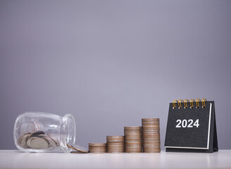 2024 desk calendar, Glass bottle with stack of coins. The concept of saving money, Financial, Investment and Business growing in new year 2024.