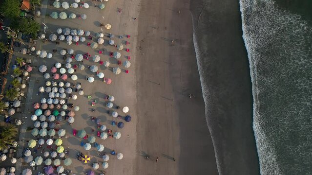 Aerial view of Beautiful sunset on the double six beach with Hotel, resort, cafe buildings, beach umbrella and calm ocean wave in Bali. Tourists are surfing, swimming and walking along the beach.