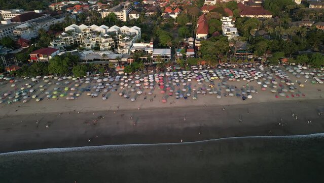 Aerial view of Beautiful sunset on the double six beach with Hotel, resort, cafe buildings, beach umbrella and calm ocean wave in Bali. Tourists are surfing, swimming and walking along the beach.