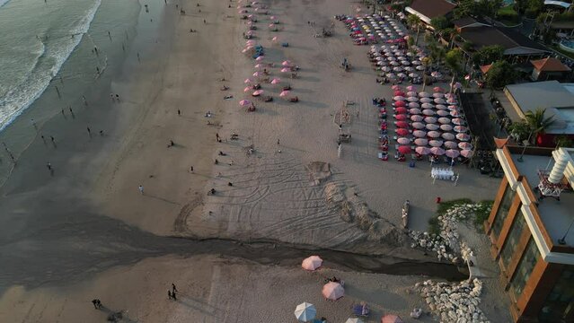 Aerial view of Beautiful sunset on the double six beach with Hotel, resort, cafe buildings, beach umbrella and calm ocean wave in Bali. Tourists are surfing, swimming and walking along the beach.