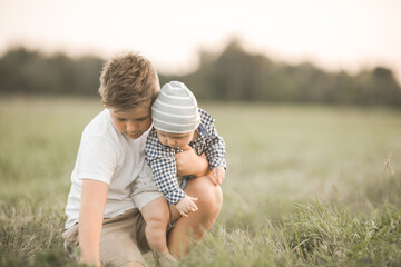 Fototapeta premium Cute boys outside, older brother hugs younger, taking care of sibling. Concept siblings and candid lifestyle