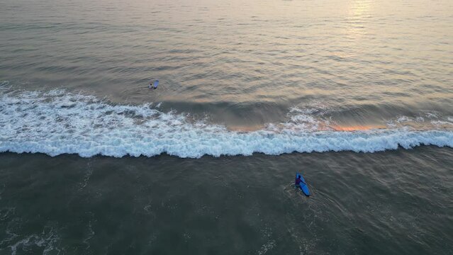 Wide angle aerial view of Tourists are surfing and swimming on the beach with ocean wave in Bali. Surfing lesson with sunset vibes. Concept for marine tourism, holiday, hobby and leisure activity.