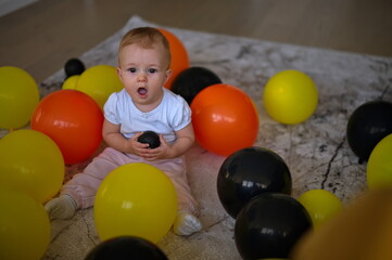 Fototapeta na wymiar Little baby girl sitting on the floor with balloons around her