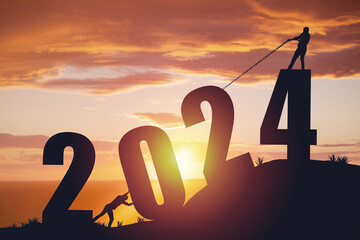 Silhouette of men pushing and pulling the year 2024 against a sunrise background