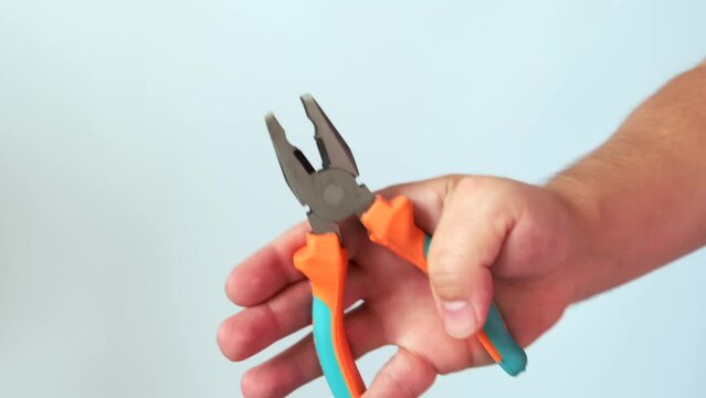Male hand holding universal pliers, work tool for repair and construction, on isolated light studio background. Close up.