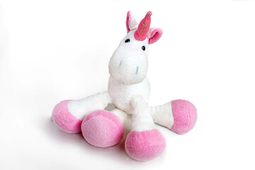Pink soft unicorn toy sitting at white background. Isolated studio image © Luci