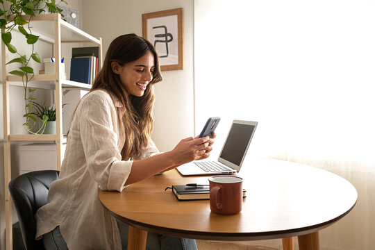Happy young woman using mobile phone working at home. Copy space.