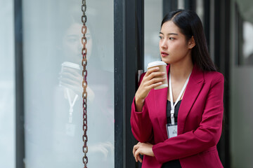 Young Asian accountant or businesswoman with a positive attitude stands holding a paper coffee cup,...