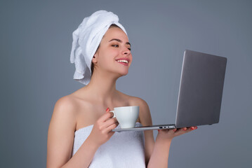 Morning freelancer working on laptop. Business woman with towel on head with coffee working on laptop. Morning coffee. Portrait of smiling woman with cup of coffee using laptop in gray studio.