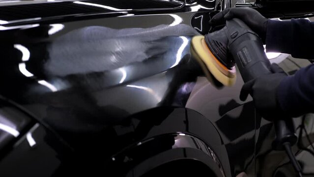 A man polishes a black car with a polishing machine in a car dealership. Car care in an auto repair shop. 