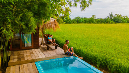 a couple of men and women in front of a Bamboo hut homestay farm, with Green rice paddy fields in Central Thailand with a small plunge pool