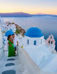 A couple of men and woman on vacation in Greece visited the village of Oia Santorini during sunset, a mature couple on a luxury holiday in Greece Santorini - obrazy, fototapety, plakaty