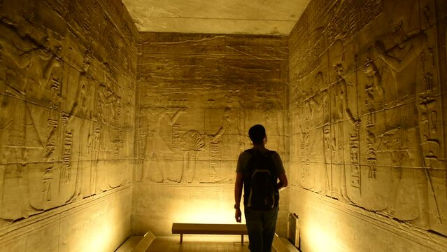 Tourist visiting inside a room of egyptian temple of Horus in Edfu Island. Traveler with a bag in egypt, visiting Horus Temple in Edfu, Egypt. Explorer, tourist watching hieroglyphs on Egypt walls