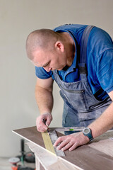 Professional tiler measuring and sticking with tape for cutting ceramic tiles for installing floor. Construction, renovation, repair apartment.