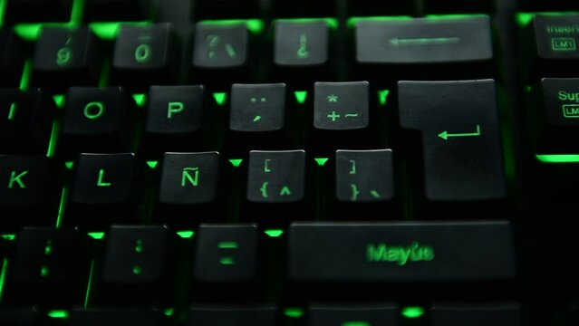 Man's hand pressing the ENTER key on a green backlit black computer keyboard. selective focus.