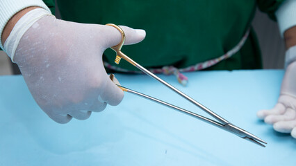 Man's hand in a white glove holding Halsey Needle Holder. This Halsey Needle Holder use for most common dissection tasks. Surgical instrument. Equipment used in surgery.