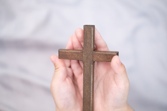 The boy's hands are holding a cross.