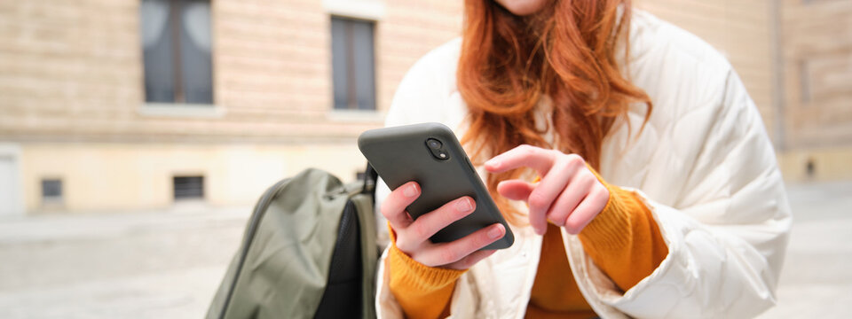 Close up of female hands typing on mobile phone, using smartphone app. GIrl with telephone types, sits outdoors and uses map