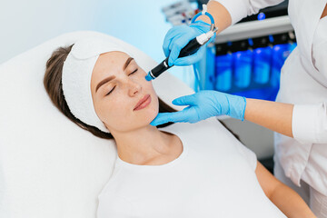 Young woman is relaxing getting vaccum facial hydro peeling procedure in beauty salon. Hardware...