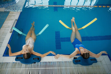 Two women doing relaxing exercise with noodles after training in swimming pool