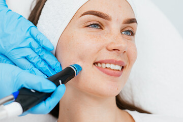 Young woman is relaxing getting vaccum facial hydro peeling procedure in beauty salon. Hardware face pores cleansing, close-up.