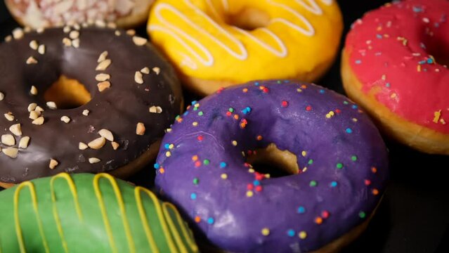 Rotating colorful donuts surface with variety glaze covered with multi-colored sprinkles on isolated black background. Bakery shop and food concept.