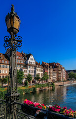 Ornate traditional half timbered houses with steep roofs above the Ill River with blooming flowers,...