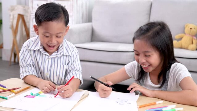 Overjoyed laughing out loud little sibling children playing drawing colorful paper together sitting on the floor, happy emotional cute boy and girl kids have fun painting pictures in a creative hobby