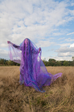 woman in a field dancing in dress with purple veil