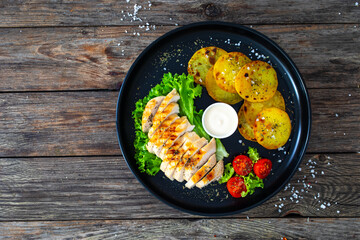 Grilled chicken breast, fried potatoes and fresh vegetables on wooden table
