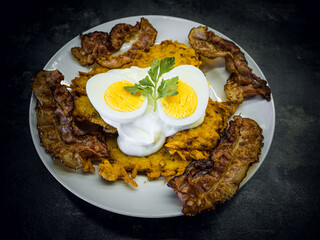 Fried bacon and boiled eggs on a white plate with dark background. Breakfast with bacon and eggs with sour cream topping.