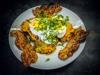 Fried bacon and boiled eggs on a white plate with dark background. Breakfast with bacon, eggs with sour cream topping and lots of parsley on top.