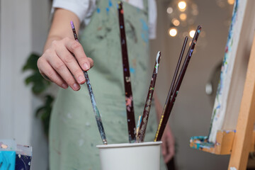 A female artist chooses an oil paint brush to paint an oil painting on canvas in her workshop.