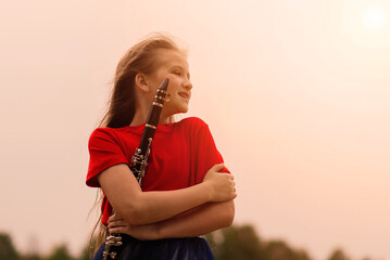 Young attractive girl playing clarinet, ebony in fall park
