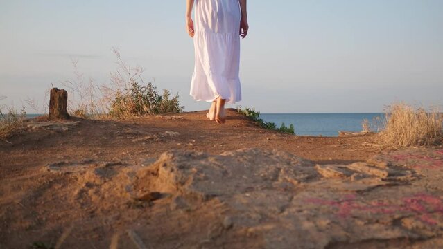 Woman walking on hill near sea at sunrise, low angle view. Camera moving