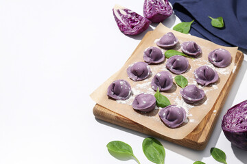 Obraz na płótnie Canvas Purple dumplings on kitchen board and cabbage on white background, space for text
