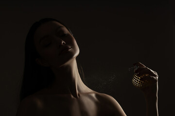 Attractive girl with perfume in her hand on a dark background